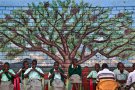 Дети на христианской мессе под открытым небом у стены с фреской, изображающей дерево, в деревне Нъюмбани, где находится приют для сирот, потерявших родителей из-за эпидемии СПИДа